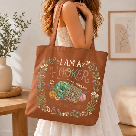 Person holding a brown tote bag with crochet-themed design and text in a home setting.