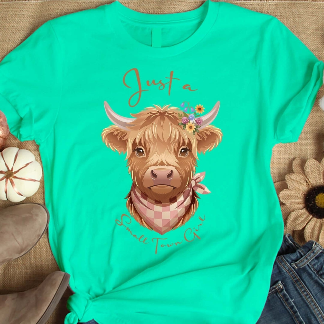 Turquoise t-shirt with a cow illustration and text on a textured surface