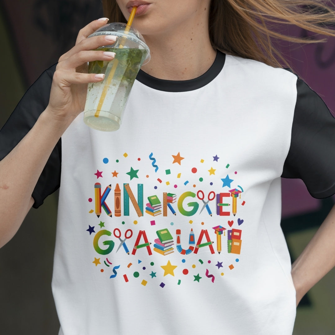 Person wearing a white t-shirt with colorful 'KINDERGARTEN GRADUATE' text, drinking from a glass.