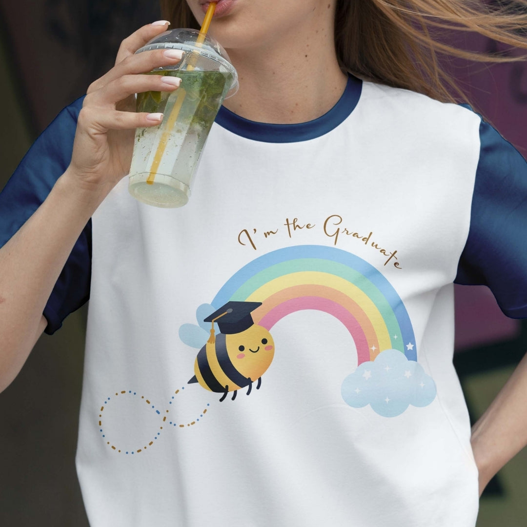 Person wearing a white t-shirt with a bee and rainbow graphic, holding a drink.
