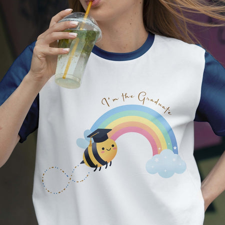 Person wearing a white t-shirt with a bee and rainbow graphic, holding a drink.