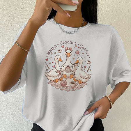 Person wearing a white t-shirt with a graphic design of ducks, text, and coffee cups.