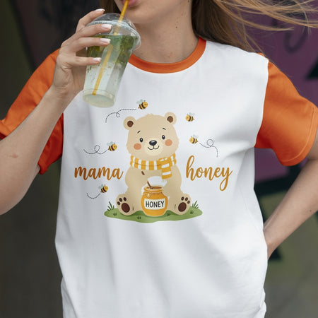 Person wearing a white t-shirt with a bear graphic and 'mama honey' text, holding a drink.