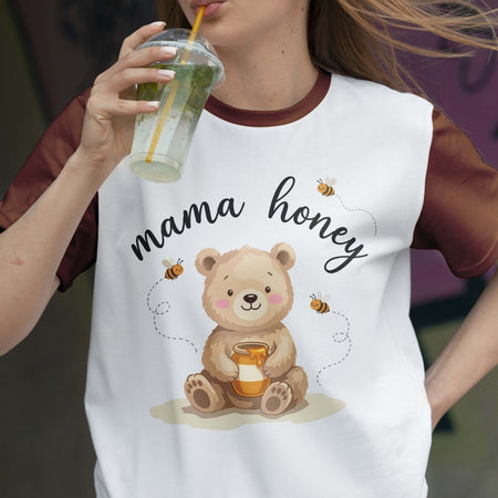Person wearing a white t-shirt with a bear graphic and 'mama honey' text, holding a drink.