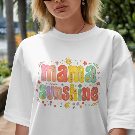 Woman with blonde hair wearing an oversized white t-shirt featuring a colorful retro "Mama Sunshine" psychedelic bubble letter print.