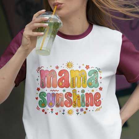 Woman drinking a refreshing beverage while wearing a retro white ringer t-shirt with maroon sleeves, printed with a colorful "Mama Sunshine" graphic.