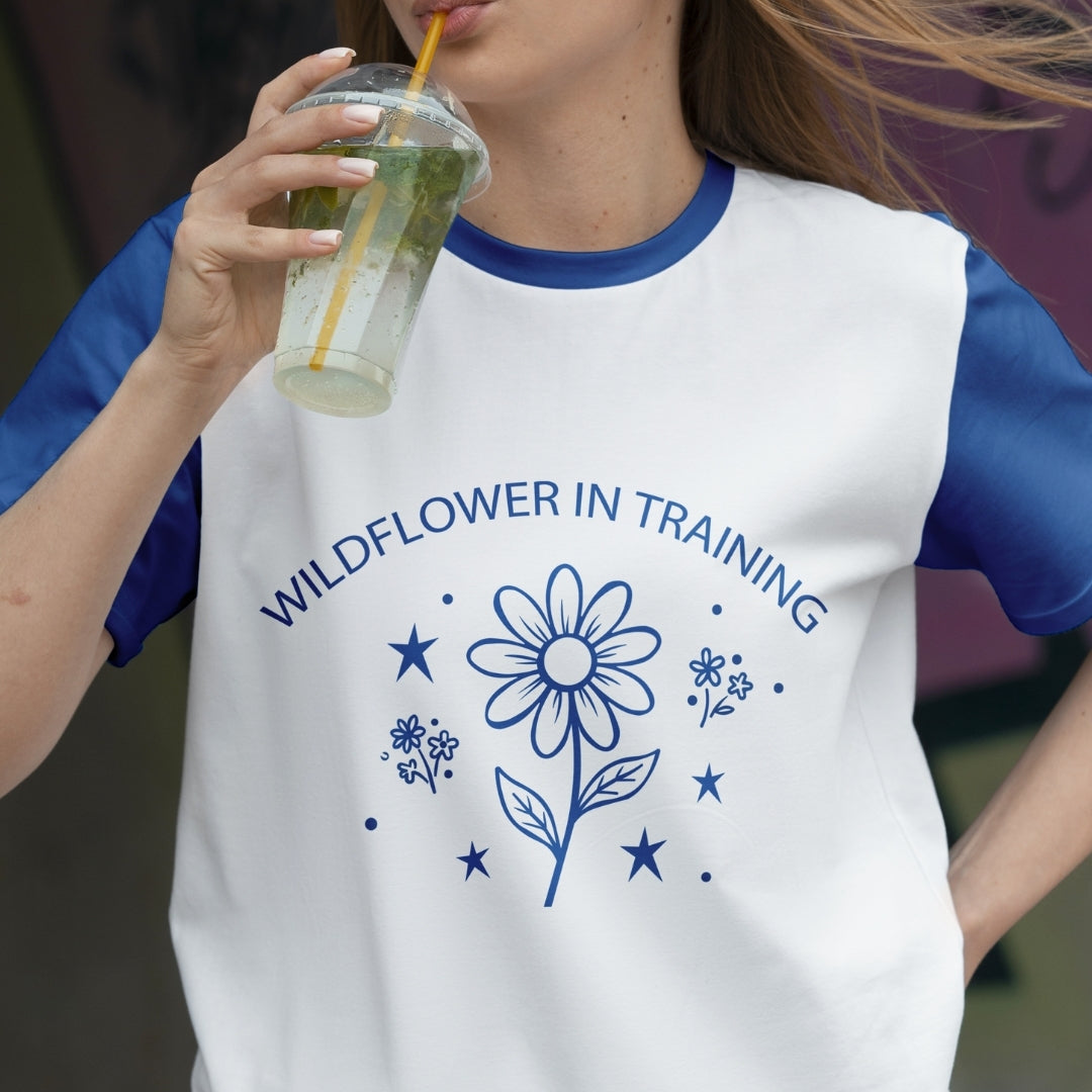 Person wearing a white t-shirt with blue floral design and text, holding a drink.