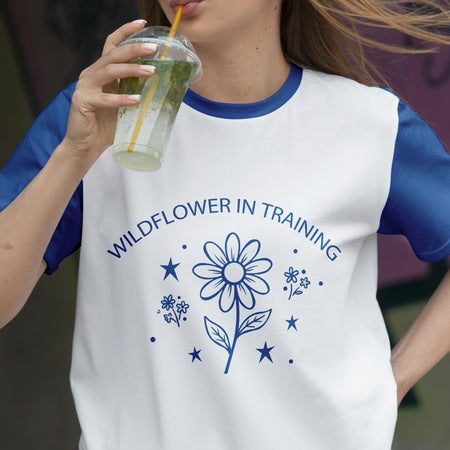 Person wearing a white t-shirt with blue floral design and text, holding a drink.