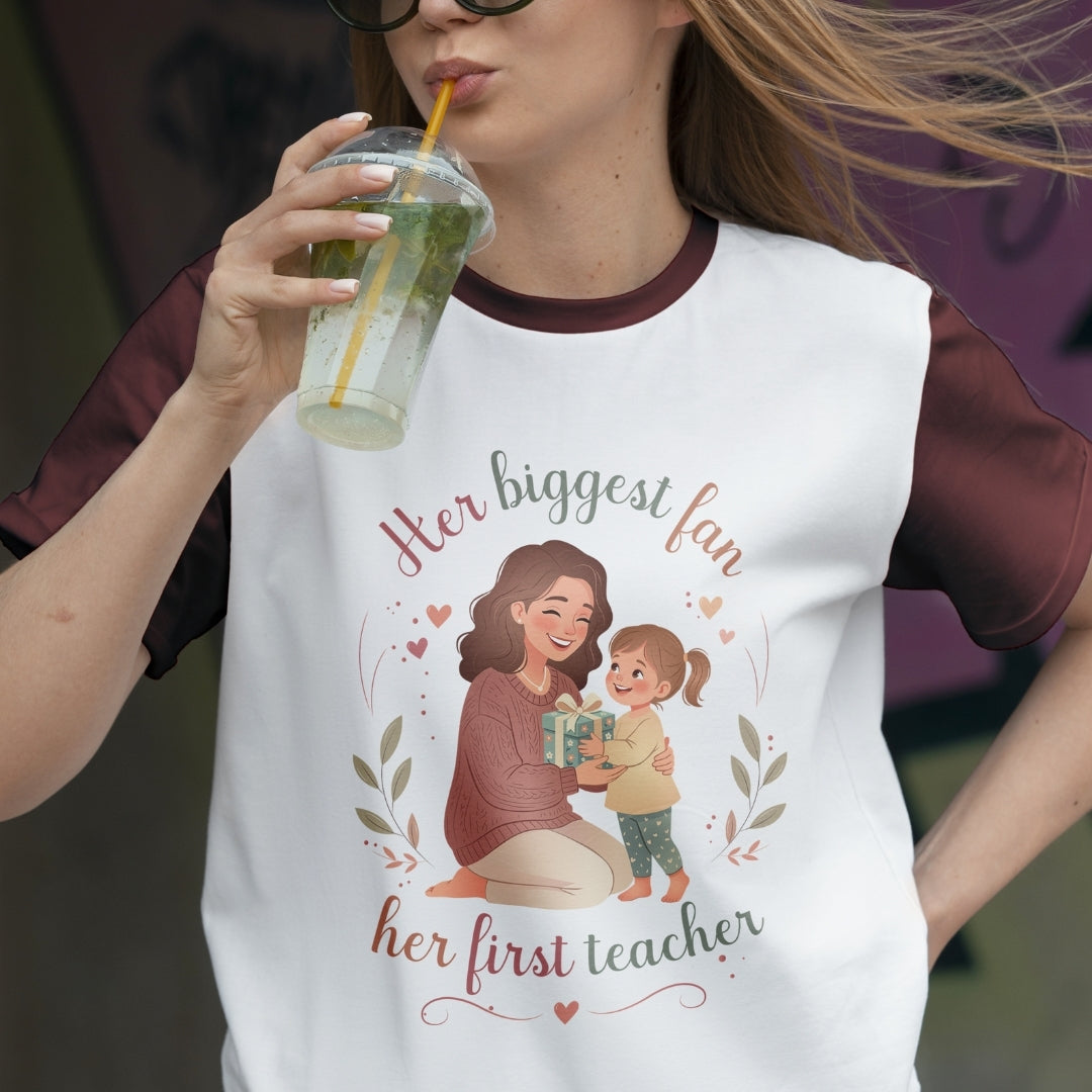 Person wearing a t-shirt with a graphic of a woman and child, and text 'Her biggest fan, her first teacher'.