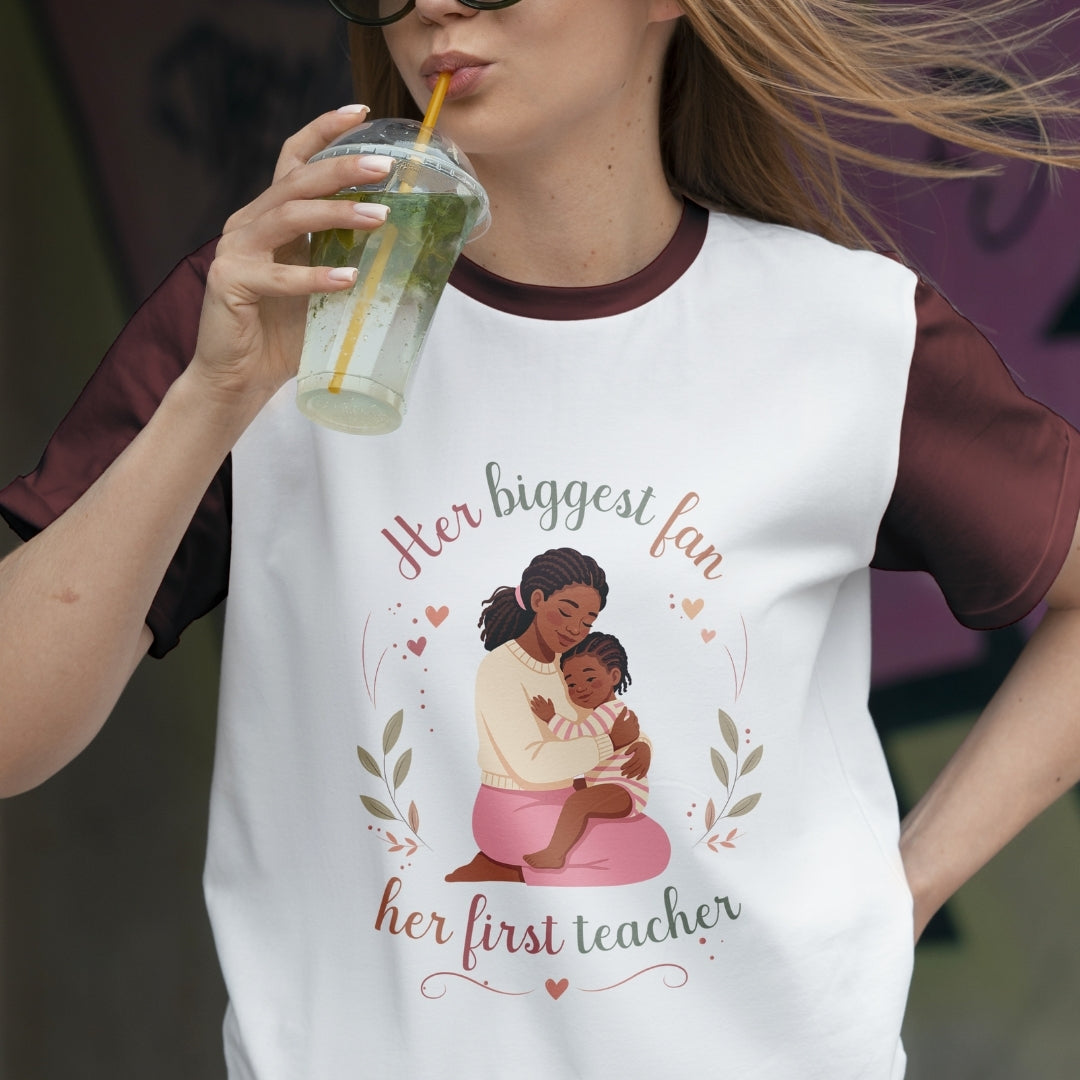 Person wearing a t-shirt with a graphic of a woman holding a child and text 'Her biggest fan, her first teacher'.
