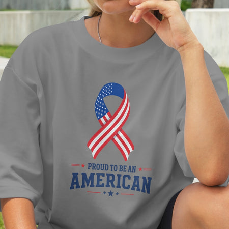 Person wearing a gray t-shirt with an American flag ribbon design and 'Proud to be an American' text.