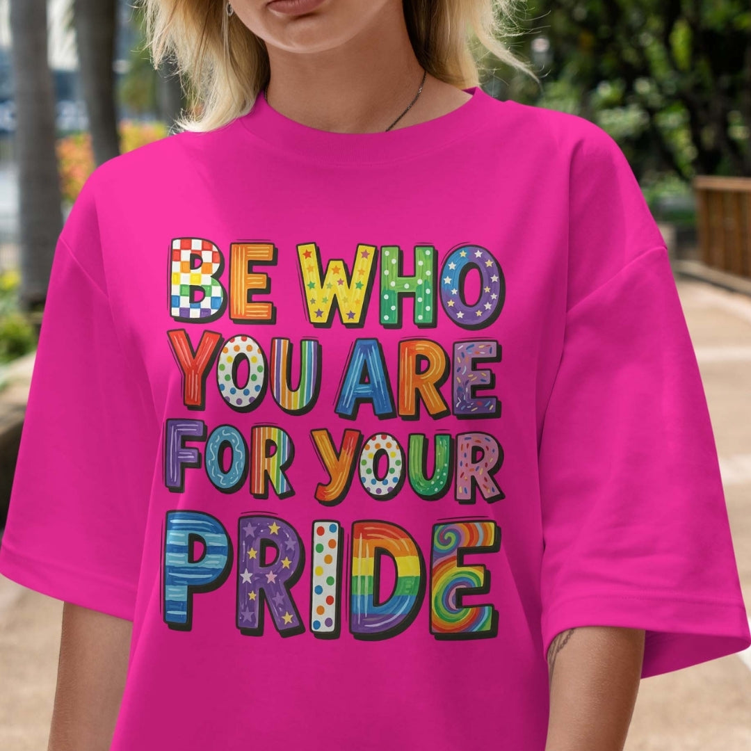 Person wearing a pink t-shirt with colorful text 'Be who you are for your pride'.
