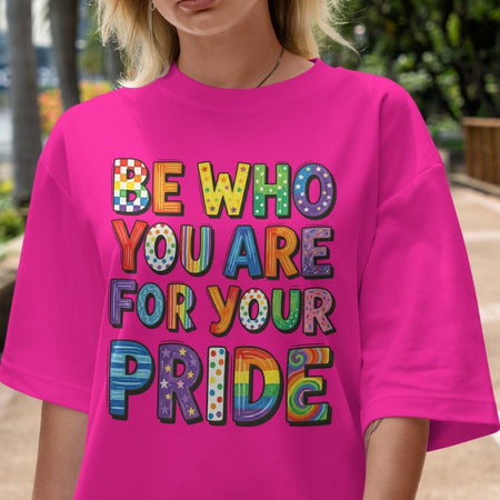 Person wearing a pink t-shirt with colorful text 'Be who you are for your pride'.