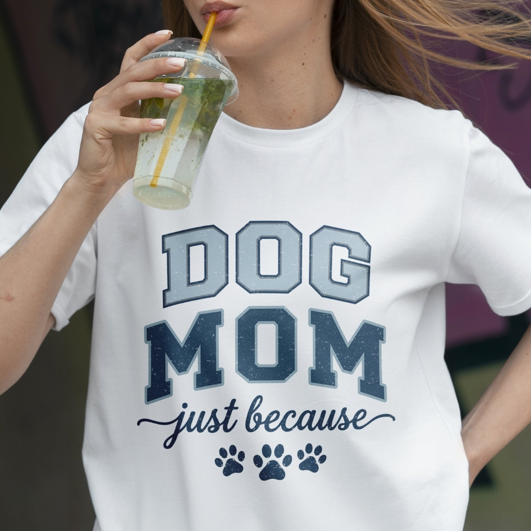Person wearing a white t-shirt with 'DOG MOM just because' text and paw prints, holding a drink.