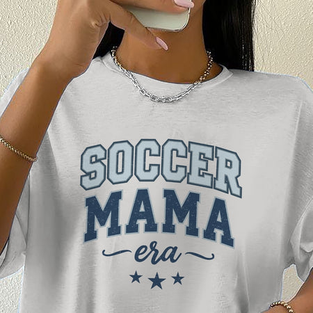 Person wearing a white t-shirt with 'Soccer Mama era' text