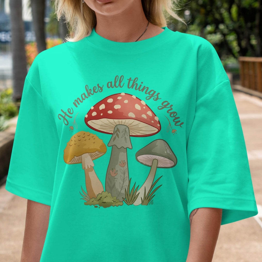 Person wearing a teal t-shirt with mushroom graphic and text outdoors