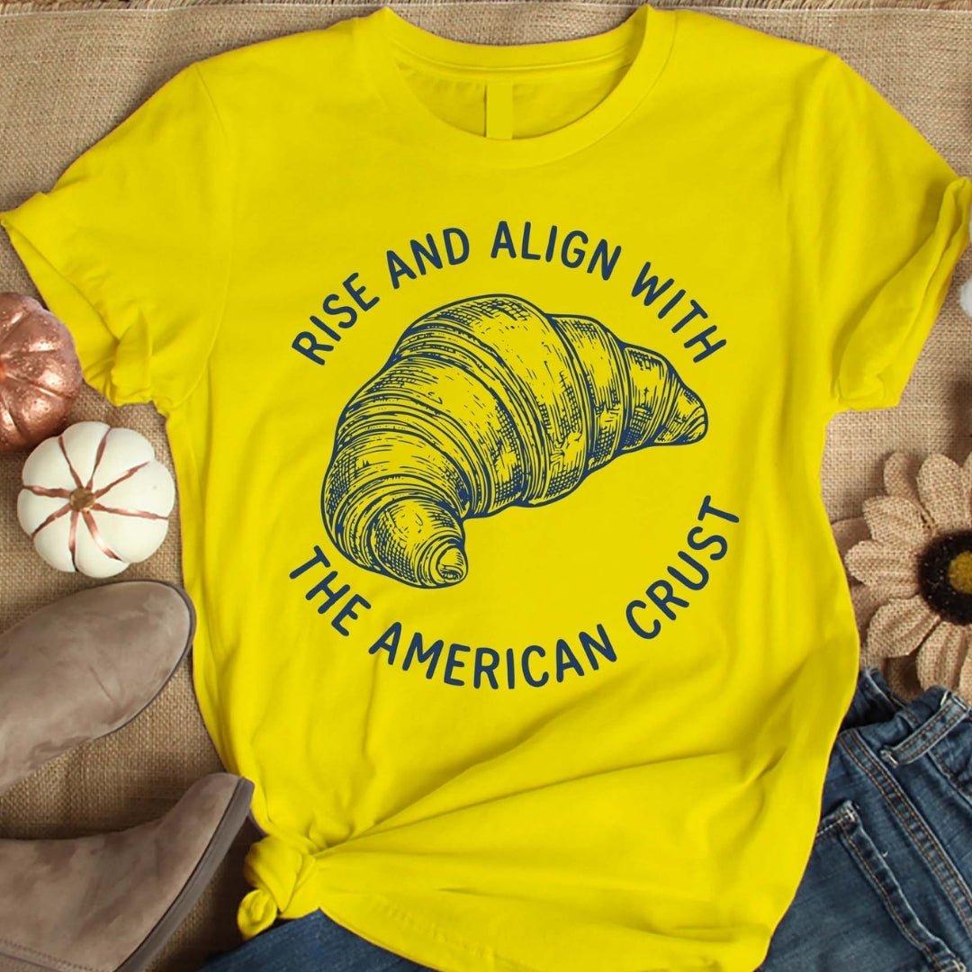 Yellow t-shirt with a croissant graphic and text on a textured surface