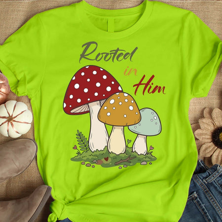 Green t-shirt with mushroom design and 'Rooted in Him' text on a textured surface.