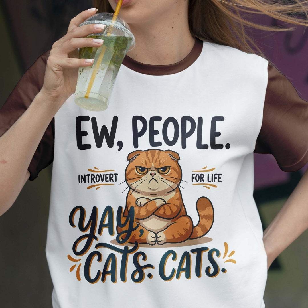 Person wearing a white t-shirt with a cat graphic and text, holding a drink.