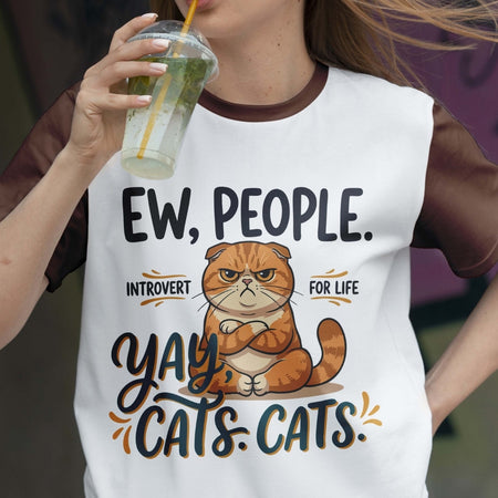 Person wearing a white t-shirt with a cat graphic and text, holding a drink.