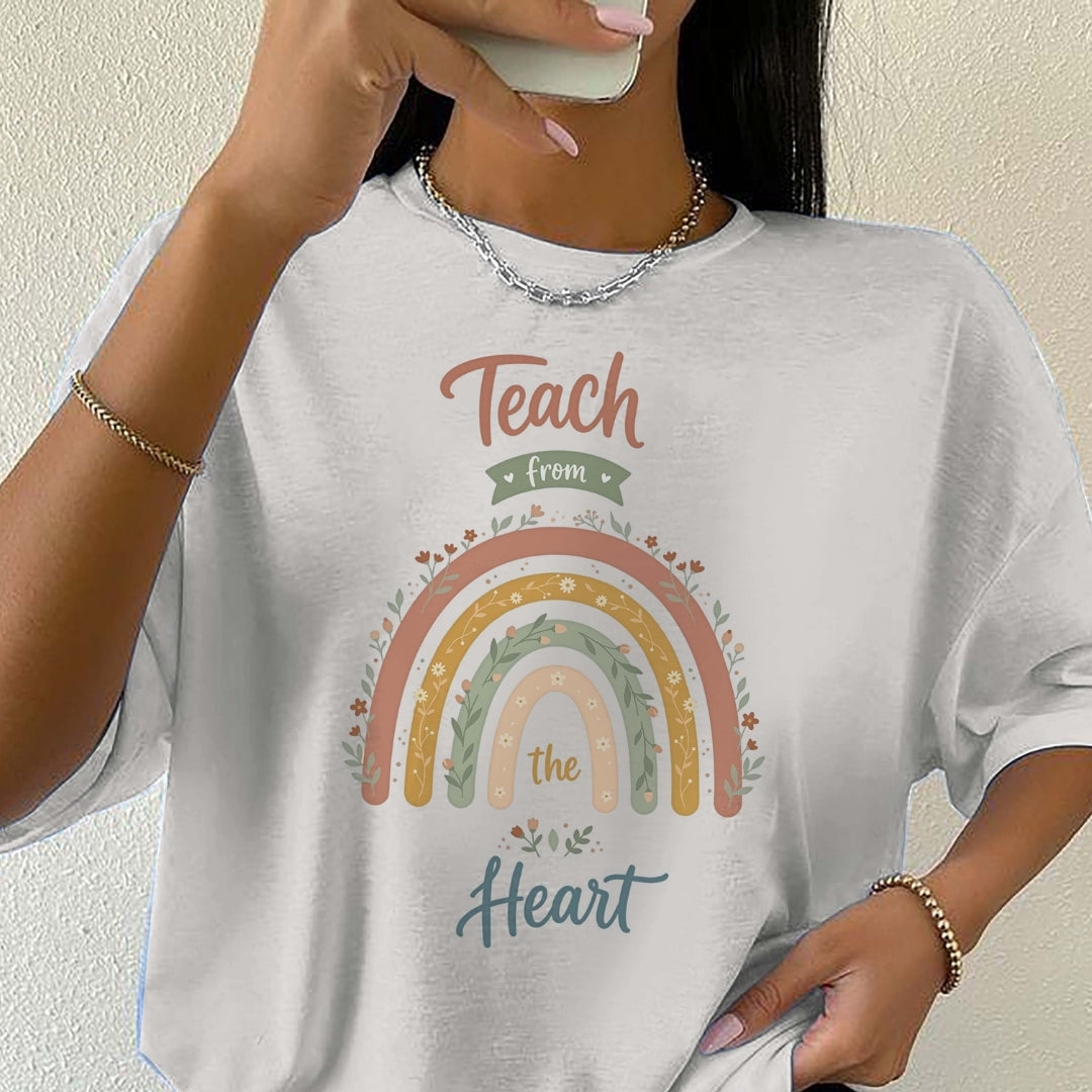 Person wearing a white t-shirt with a rainbow and text design, holding a phone.