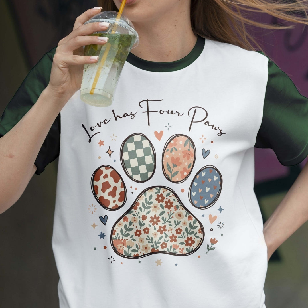 Person wearing a white t-shirt with paw print designs and text, holding a drink.