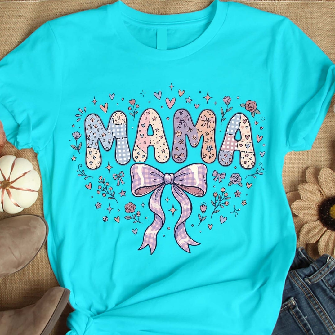 Turquoise t-shirt with 'MAMA' design featuring a bow and flowers on a wooden surface.